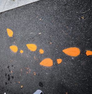 Orange Hand in Stopphaltung mit den Worten Stopp Gewalt an Frauen. Daneben orange Schuhabdrücke.